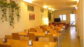 A dining area with multiple tables and chairs, a television, and hanging plants. - Hostel Albergue Studio (Barcelona)