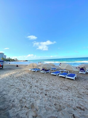 A beach with sun loungers and umbrellas, a clear sky, and a calm sea. - Condado Serenity by the Sea 2Bd/2Bth wth Parking (San Juan)