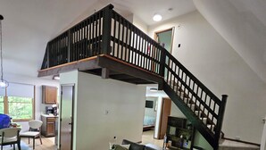 Un salón amplio con un sofá seccional grande, un reposapiés pequeño y una escalera que sube a un nivel superior.