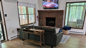 Amplia sala de estar con chimenea, televisor montado arriba y un ventanal que proporciona luz natural.