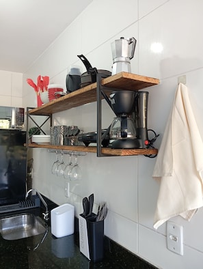 Une cuisine avec une étagère en bois où sont posées des casseroles, une machine à café et une serviette suspendue.
