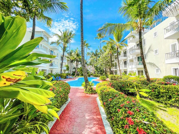 A resort with a swimming pool, palm trees, and a red pathway. - DELUXE STUDIOS HOTEL POOL AND BEACH (Punta Cana)