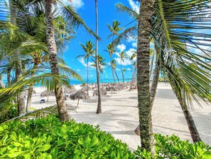 A beach with palm trees and thatched umbrellas. - DELUXE STUDIOS HOTEL POOL AND BEACH (Punta Cana)