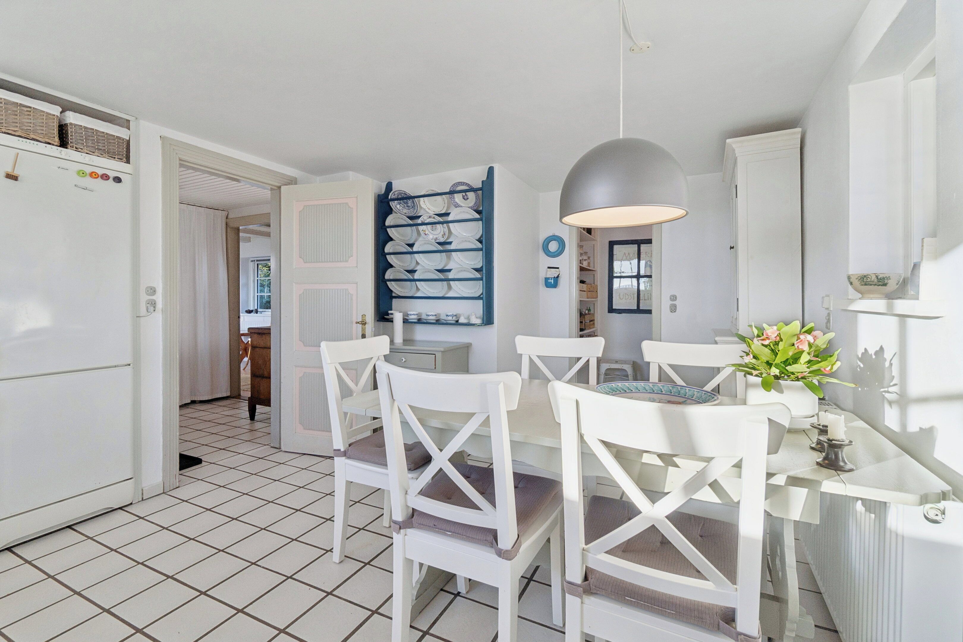 A kitchen with white chairs, a dining table, a blue dish rack, and a pendant light.
