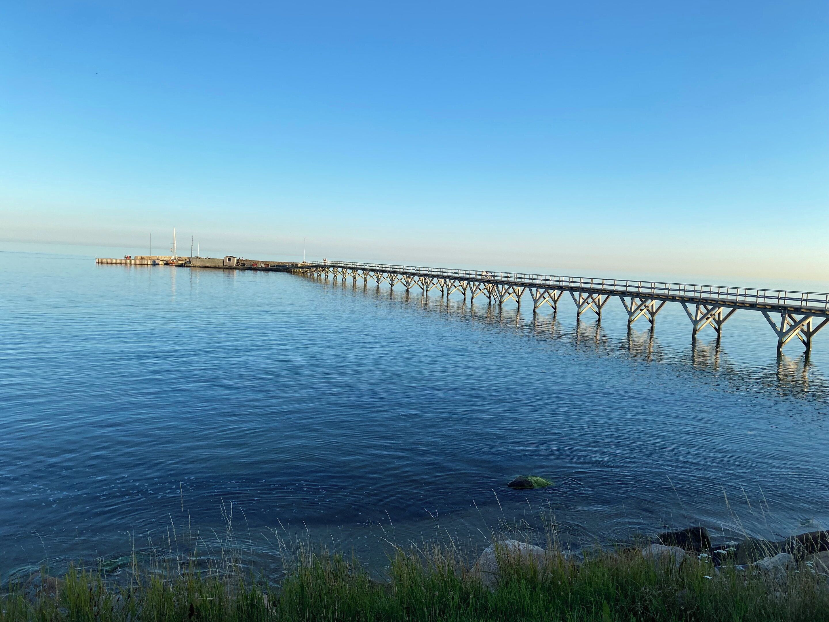 Une jetée s’avançant dans une eau calme, sous un ciel dégagé.