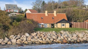 Ein Küstenhaus mit rotem Ziegeldach, einer Steinmauer und Blick auf das Meer.