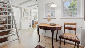 Ein Zimmer mit Holzboden, einem runden Holztisch, einem Holzstuhl, einem weißen Bücherregal und einer Leiter.