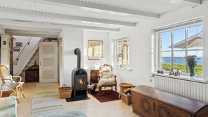 Ein gemütliches Zimmer mit Kamin, Korbmöbeln, einer hölzernen Bank und Meerblick.