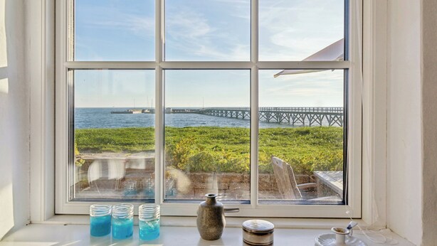 Ein Fenster mit Blick auf einen Steg und Wasser, eine Vase sowie drei Gläser auf einem Fensterbrett.