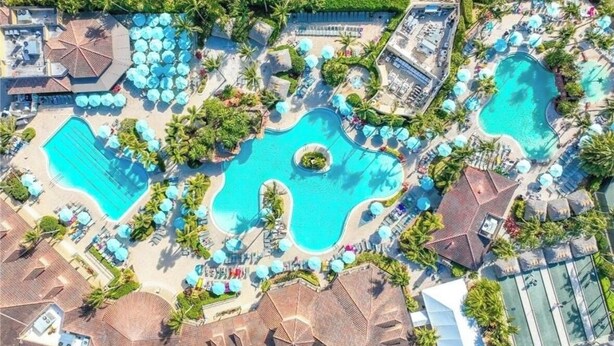 Vista aérea de un complejo turístico con varias piscinas, sombrillas de sol y zonas de descanso.