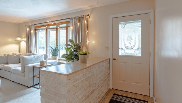 Sala de estar con un sofá, una mesa de centro y una planta en maceta. Se ve una puerta con un panel de vidrio y cortinas.