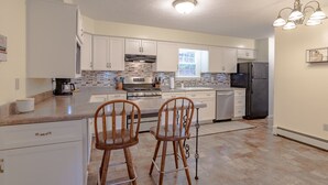 Una cocina moderna con armarios blancos, una estufa de acero inoxidable, un refrigerador y dos taburetes de madera para bar.