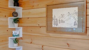 Un mur en bois, agrémenté d’étagères où sont disposées des plantes en pot, et sur lequel est accroché un dessin encadré représentant un paysage de montagne.