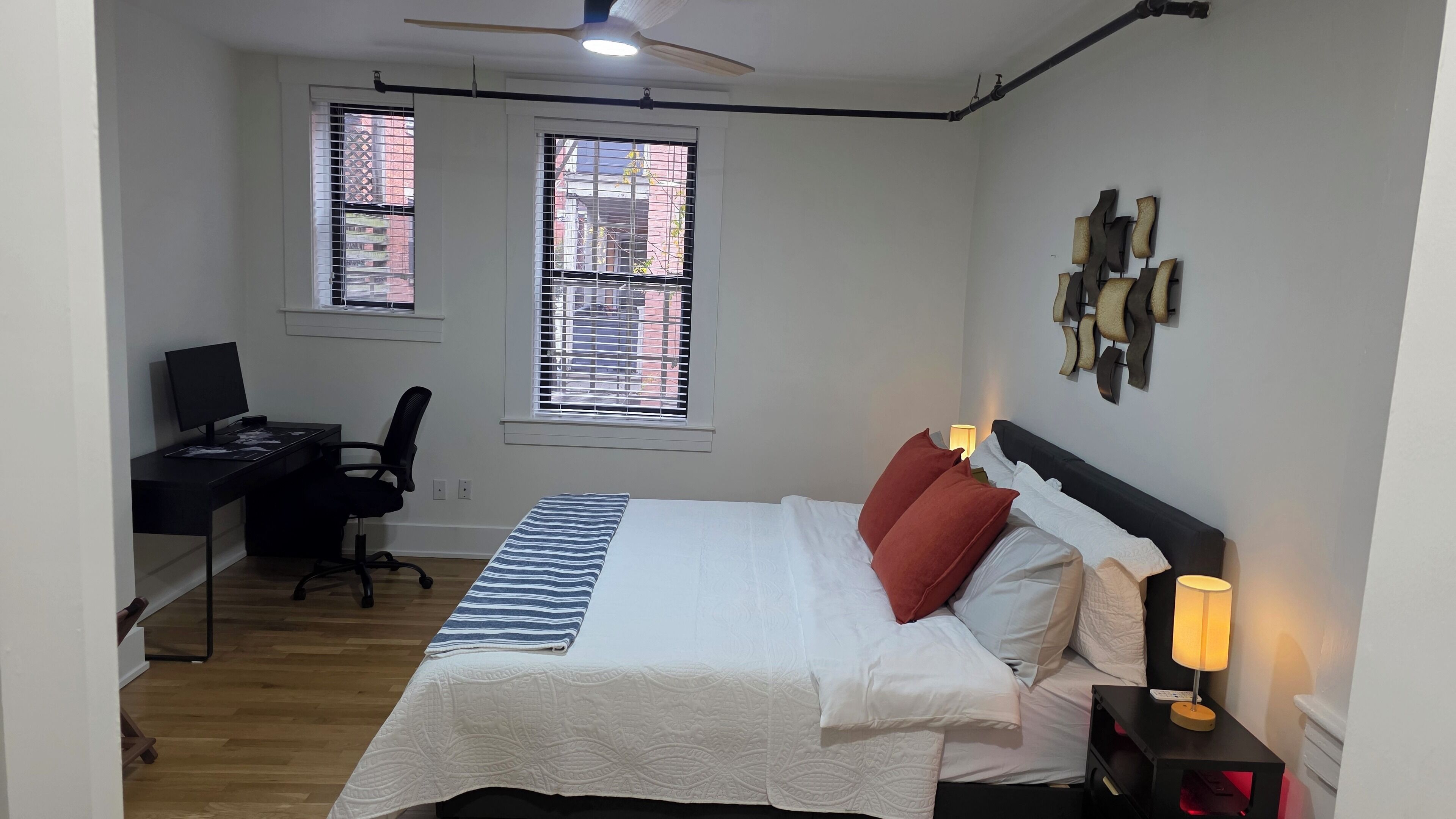 A bedroom with a bed, desk, chair, and two windows.