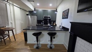 A modern kitchen with a central island, stainless steel appliances, and a black countertop. - Quiet cheerful condo in the heart of OTR! (Cincinnati)