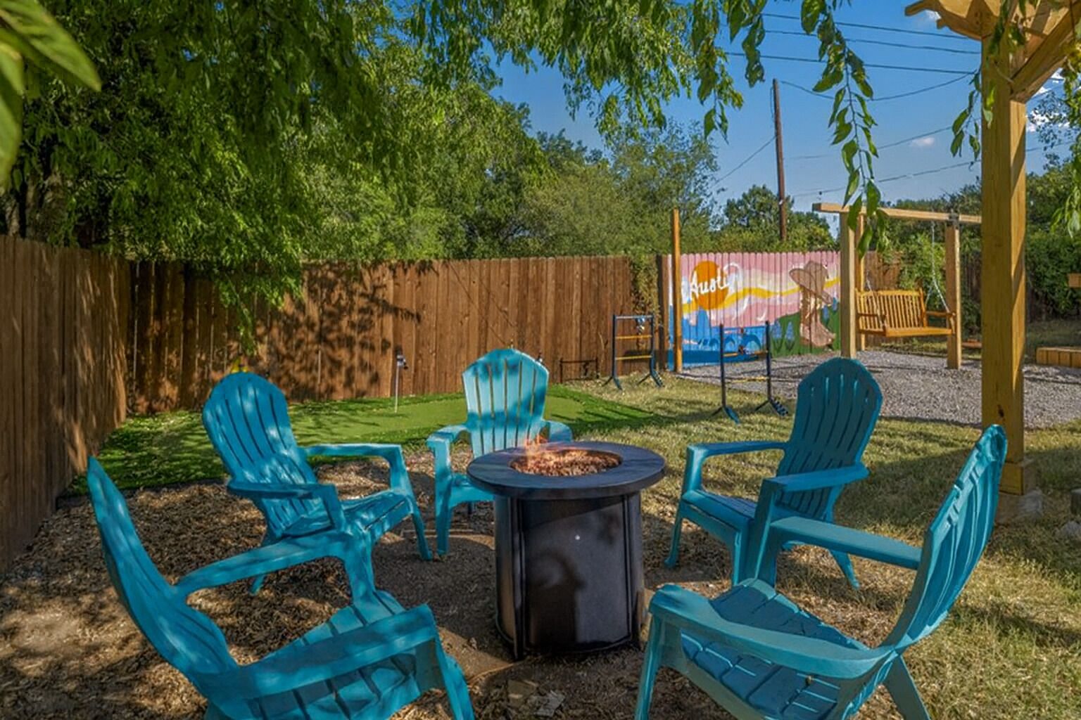 A backyard with a fire pit, four blue Adirondack chairs, and a wooden fence.