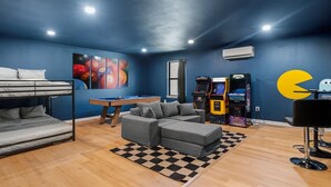 A room with a pool table, a sofa, a bunk bed, and arcade machines. - Poolside Paradise Room Fire Pit Hot Tub (Round Rock)