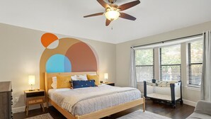 A bedroom with a bed, bedside tables, a ceiling fan, and a window with blinds. - Poolside Paradise Room Fire Pit Hot Tub (Round Rock)