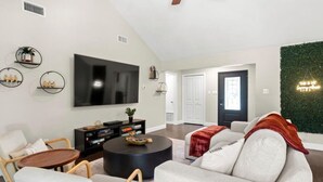 A modern living room with a flat-screen TV, comfortable seating, a ceiling fan, and a green wall accent. - Poolside Paradise Room Fire Pit Hot Tub (Round Rock)