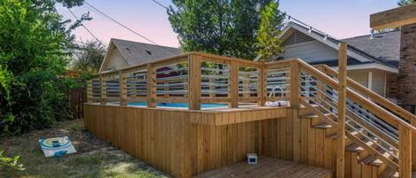 A wooden deck with a pool, a wooden staircase, and a target on the ground.