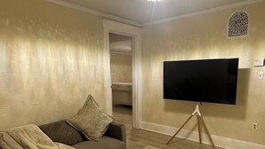 Un salon avec un canapé, un téléviseur posé sur un pied, et un tapis à motifs.