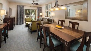 Habitación de hotel con comedor, sofá, televisor y balcón con cortinas.