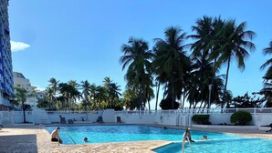 Un espace piscine doté d’un sol en pierre, de palmiers et d’une clôture blanche.