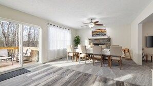 Ein geräumiges Wohnzimmer mit einer großen Glasschiebetür, die auf eine Terrasse führt, einem Essbereich mit Kamin und Deckenventilator.