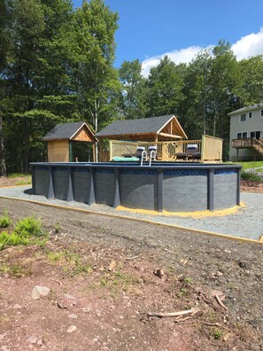 A cabin with a deck, a covered area with seating, and a swimming pool. - Heated Pool/4 Bedroom 3 Bath Home/Hot Tub/Fire Pit/Large Game Room/PS5! (Pocono Lake)