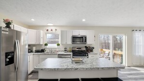 Eine moderne Küche mit weißen Schränken, einer Arbeitsplatte aus Granit, einem Edelstahlkühlschrank und einer großen Kochinsel mit Barhocker.