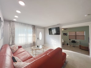 Ein Wohnzimmer mit einem roten Ledersofa, einem Glastisch und einem an der Wand befestigten Flachbildfernseher.