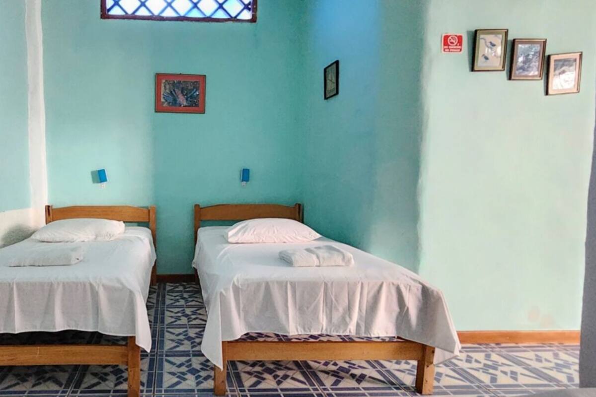 A room with two single beds, a tiled floor, and a window with a lattice design.