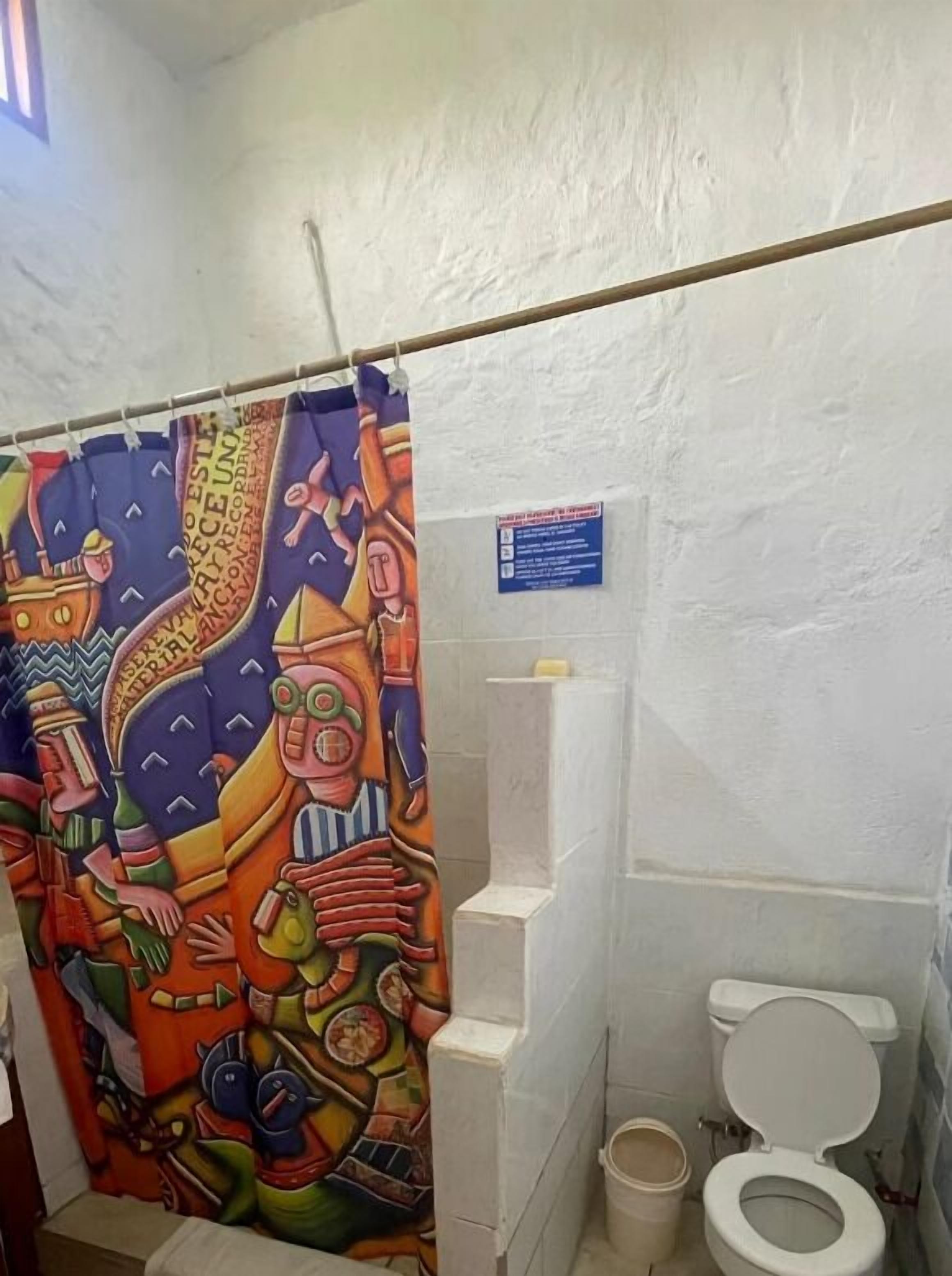 Un baño con cortina de ducha colorida, un inodoro blanco y una pequeña estantería con artículos de aseo.