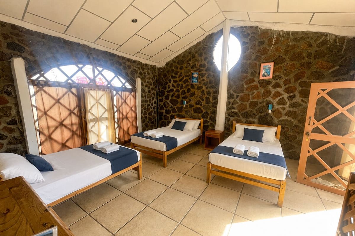 A room with three beds, a stone wall, a wooden door, and a window with a view.
