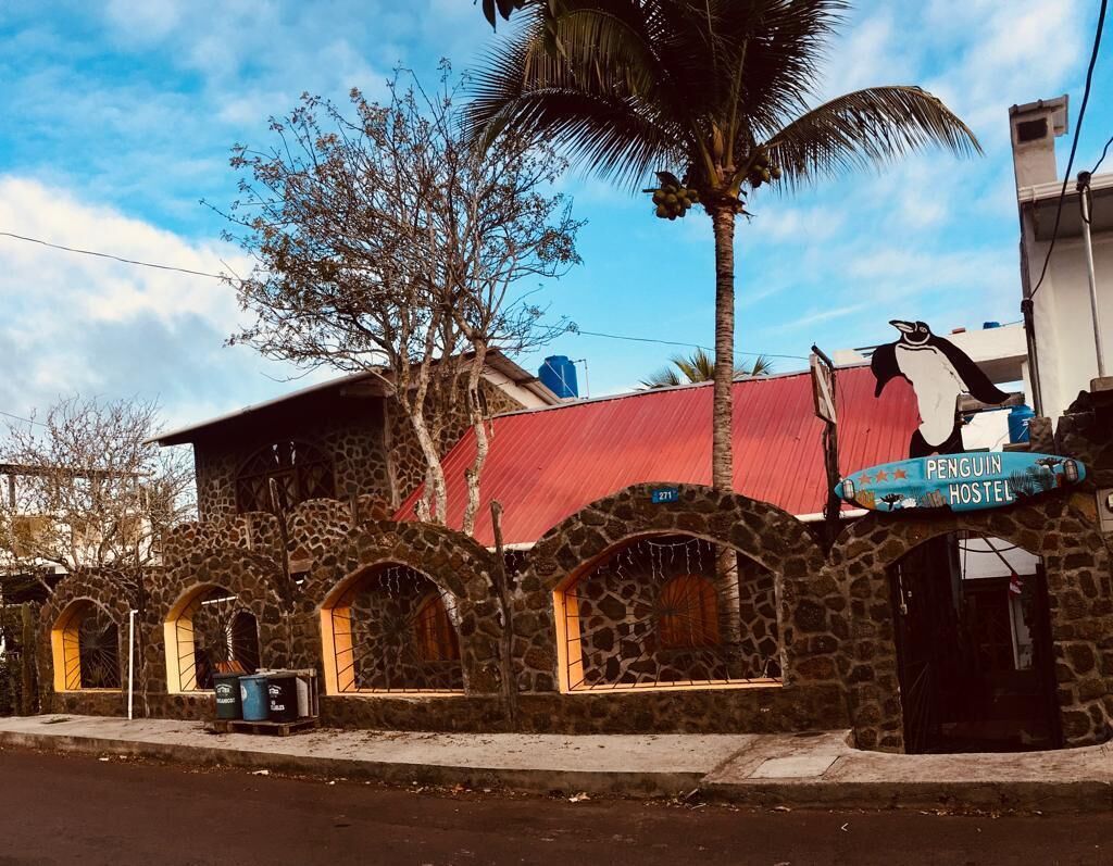 Um edifício de pedra com janelas em arco e telhado vermelho, identificado como 'Penguin Hostel'.