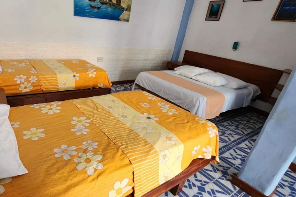A room with two beds, each with a floral bedspread and white pillows. There is a painting on the wall above the beds and a patterned floor.
