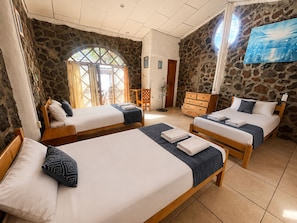 Habitación de hotel con tres camas de madera, paredes de piedra, un ventanal grande y un televisor de pantalla plana.