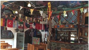 A restaurant with wooden tables and chairs, a stone counter, and various flags hanging from the ceiling. - PENGUIN HOSTEL (Puerto Ayora)