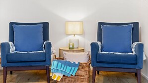 Dos sillones azules con detalles blancos, una mesita redonda con una lámpara, una cesta de mimbre y un plaid de colores azul y amarillo.