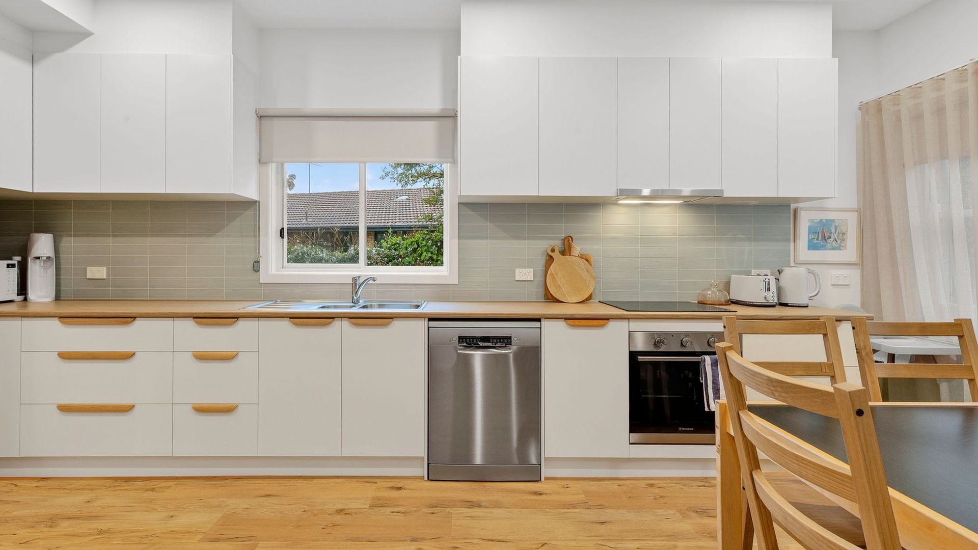 Una cucina moderna con mobili bianchi, lavastoviglie in acciaio inossidabile, forno integrato e una finestra vista verde.