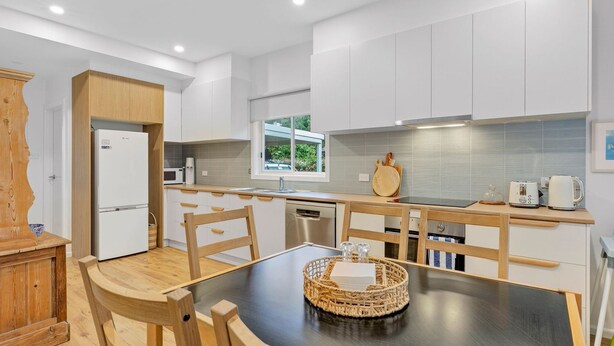 Una cocina moderna con armarios blancos, una mesa de comedor de madera y vistas a zonas verdes al exterior.