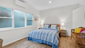 Un dormitorio con cama, mesitas de noche, lámpara, una silla de mimbre y una ventana con vidrio esmerilado.
