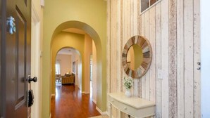 A hallway with a wooden wall, a round mirror, and a white console table. - Near Disney Cozy 3Bd Apartment at Caribe Cove (Kissimmee)