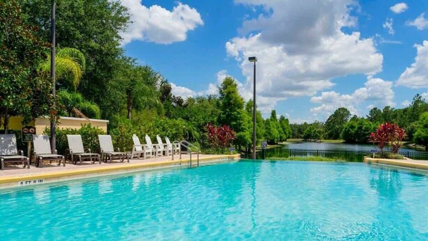 A swimming pool with lounge chairs, a small pond, and lush greenery. - Near Disney Cozy 3Bd Apartment at Caribe Cove (Kissimmee)
