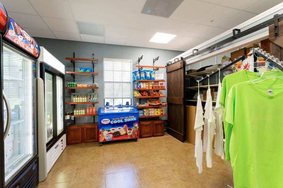 Een klein winkelgedeelte met een koelvitrine, planken vol snacks en een kledingrek.