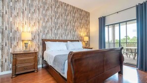 A bedroom with a wooden headboard, a wooden wall panel, two bedside tables with lamps, and a view through a large window. - Near Disney Cozy 3Bd Apartment at Caribe Cove (Kissimmee)