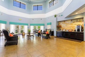 Eine geräumige Lobby mit hohen Decken, einer zentralen Sitzgruppe, einer Rezeption und einer großen Wandkarte.