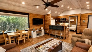 A cozy cabin interior with a dining area, a bar, a sofa, and a television. - Private Wooded Cabin w/ Hot Tub, Fire Pit. 5 minutes from Texas A&M (Navasota)