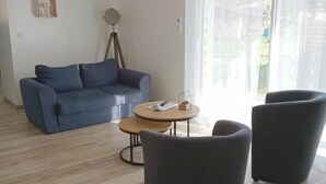 Ein modernes Wohnzimmer mit einem blauen Sofa, zwei Sesseln, einem kleinen runden Tisch und einer Stehlampe.
