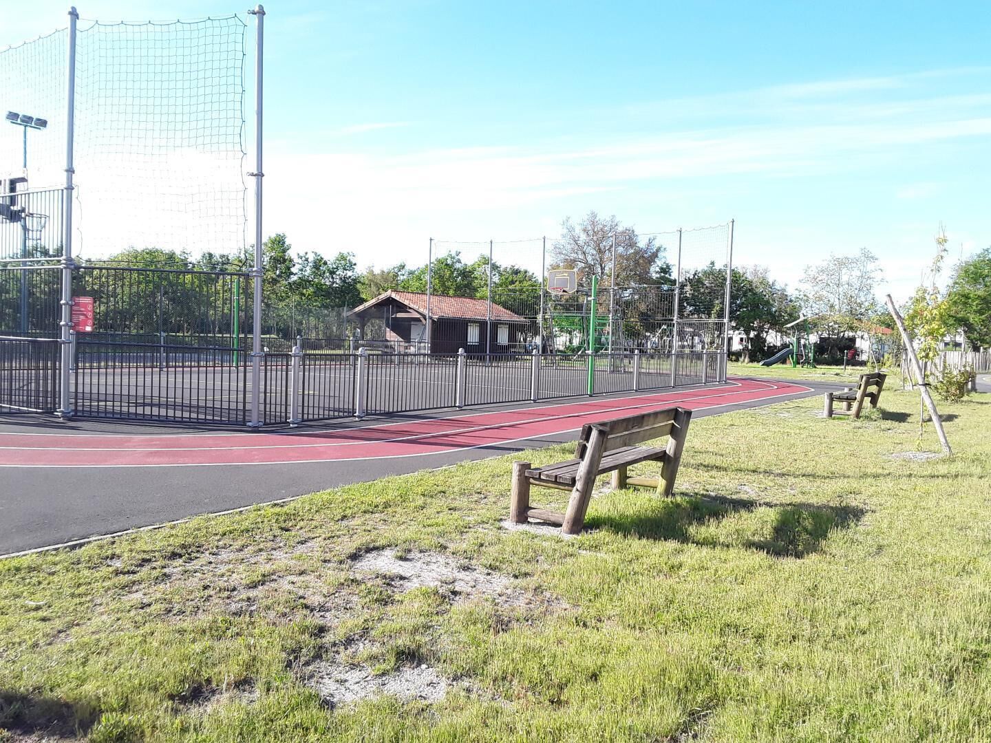 En sportplan med en röd löparbana, omgiven av ett staket av metall och ett litet skydd.